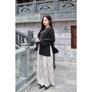May include: A long-sleeved black jacket with a row of white buttons and side slits, paired with high-waisted, wide-leg trousers featuring a light gray and white floral pattern. The outfit is completed with simple black pointed-toe flats.