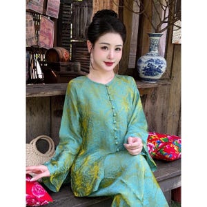 Puede incluir: Un conjunto de dos piezas con estampado turquesa y amarillo, con mangas largas y detalles de botones. El conjunto lo lleva una persona con cabello oscuro. También se ven un bolso de paja y un cojín floral rojo.