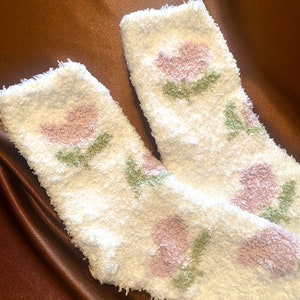 May include: A pair of white fuzzy socks with a pink and green floral pattern.
