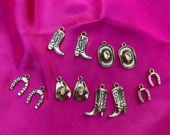 May include: A collection of 10 gold-toned metal charms with western themes. The charms include cowboy boots, horseshoes, hats, and a horseshoe with the words "good luck" on it.