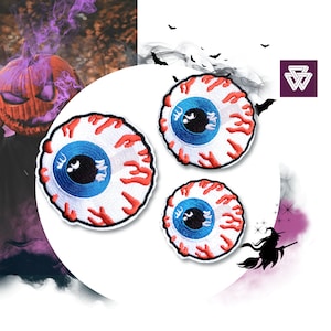 Könnte beinhalten: Drei gestickte Bügelbilder mit einem blauen Auge, um das rote Tropfen verlaufen. Das Auge hat eine schwarze Pupille und eine weiße Sklera.