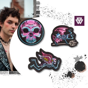 May include: Three embroidered iron-on patches featuring a pink and blue skull, a pink and blue skeleton with wings, and a pink and blue skeleton with wings and a trident.
