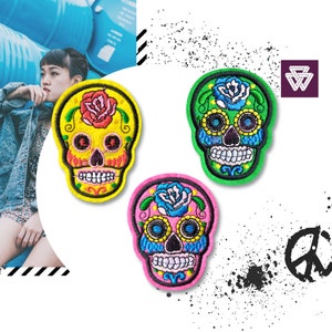 May include: Three embroidered sugar skull patches in pink, yellow and green. Each skull has a flower design and colourful details.