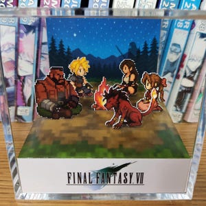 May include: A pixel art diorama featuring characters from Final Fantasy VII gathered around a campfire under a starry night sky. The diorama is encased in a clear acrylic block, with the game's logo displayed on the front.