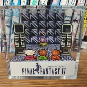May include: A clear acrylic display case with a miniature diorama of a video game scene. The scene features four pixelated characters standing in front of a large, black, pixelated structure. The text "FINAL FANTASY IV" is printed on the base of the display case. The text "ファイナルファンタジーIV" is printed in Japanese above the English text.