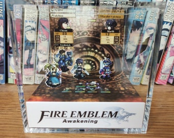 May include: A clear acrylic cube display case with a 3D image of characters from the video game Fire Emblem: Awakening. The image includes the characters Chrom, Frederick, Marth, and a fourth character. The case has a white base with the game's logo and title, "Fire Emblem: Awakening".