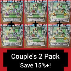 May include: Two sets of Pokemon themed 3D dioramas in clear acrylic boxes. Each set features a couple of Pokemon characters and a heart. The boxes have a green background and a white label with the text "Training together since" and a date. The text "Couple's 2 Pack Save 15%+!" is at the bottom of the image.