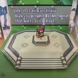 May include: A green, pixelated, 3D pop-up of Link from the Legend of Zelda video game series. Link is holding a sword and standing on a platform with a green background. The text "Link, it is extraordinary that you won the Master Sword that makes evil retreat..." is visible in the background.