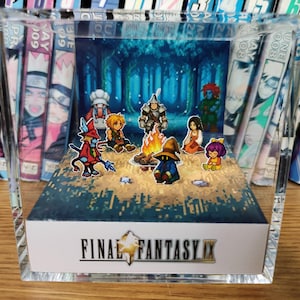 May include: A clear acrylic display featuring a scene from Final Fantasy IX. The diorama shows several cartoon characters gathered around a campfire in a forest setting. The words "FINAL FANTASY IX" are printed on the base.