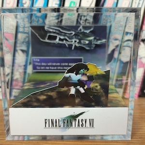 May include: A clear plastic cube with a 3D pop-up scene from the video game Final Fantasy VII. The scene features two characters, Cloud Strife and Tifa Lockhart, standing on a grassy hill. The text "FINAL FANTASY VII" is printed on the base of the cube.
