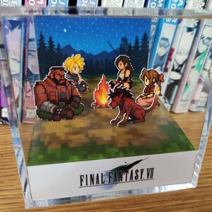 May include: A clear acrylic display featuring a pixelated scene from Final Fantasy VII. The scene depicts characters around a campfire under a starry night sky. The Final Fantasy VII logo is at the bottom.