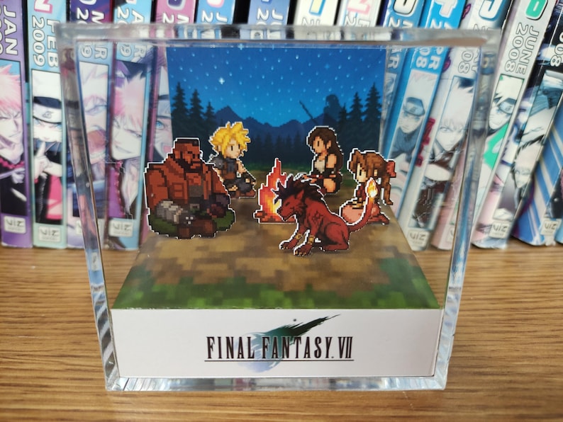 May include: A clear acrylic display featuring a pixelated scene from Final Fantasy VII. The scene depicts characters gathered around a campfire under a starry night sky. The Final Fantasy VII logo is displayed on the front.