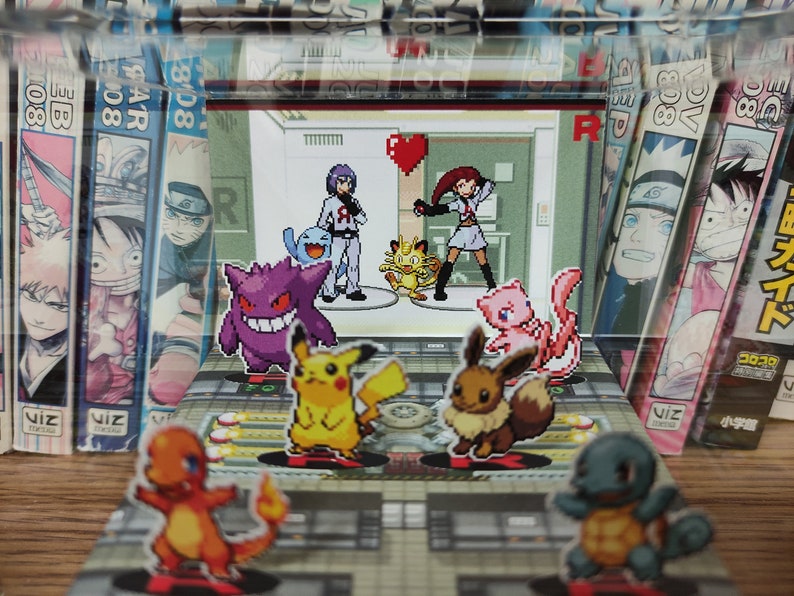 Puede incluir: Una colecci&oacute;n de figuras de Pok&eacute;mon, incluyendo Pikachu, Charmander, Squirtle, Bulbasaur y un entrenador, expuestas en un tablero de juego con un fondo de libros de manga de anime.