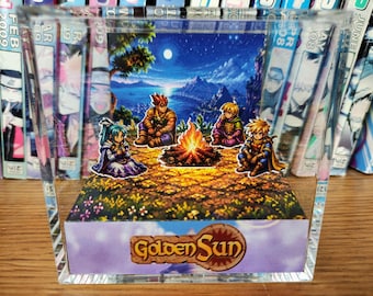 Puede incluir: Una pantalla acrílica transparente con una escena de Golden Sun. La obra de arte representa a cuatro personajes reunidos alrededor de una fogata bajo un cielo iluminado por la luna. El logotipo de Golden Sun es visible en la parte inferior. Volúmenes de manga en el fondo.