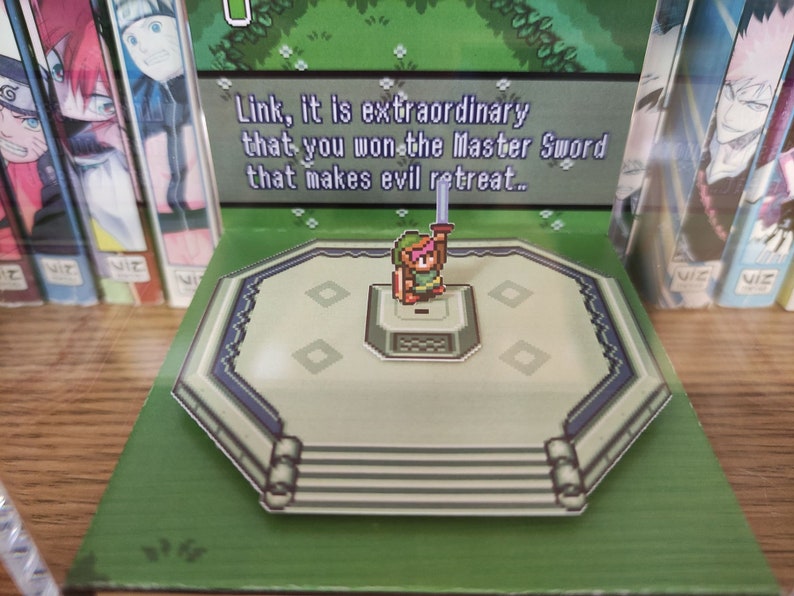 May include: A pop-up book featuring a pixelated character holding a sword. The text reads "Link, it is extraordinary that you won the Master Sword that makes evil retreat..."
