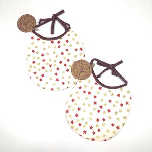 May include: Two white bibs with red and gold stars. The bibs have brown ties and a brown trim. Each bib has a small brown tag with a design on it.