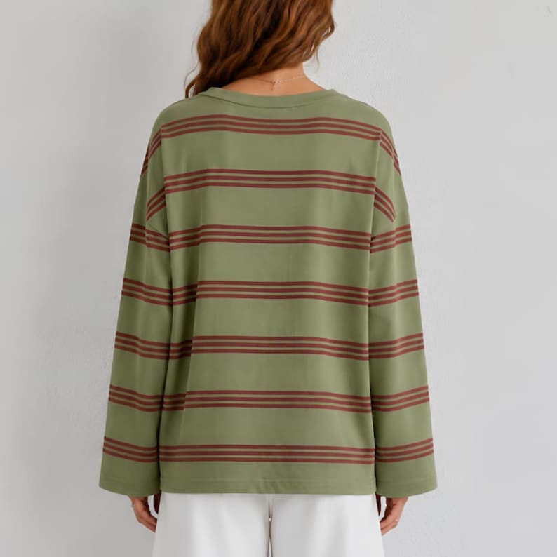 May include: A long-sleeve shirt in a muted olive green color featuring horizontal stripes in a dark reddish-brown tone. The garment has a crew neckline and a relaxed, loose fit, with the striped pattern continuing across the sleeves and back.