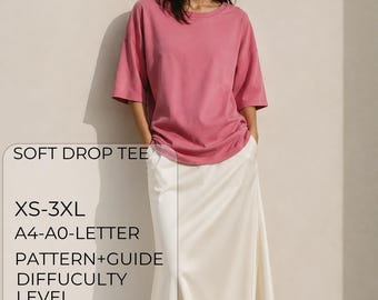 Puede incluir: Una camiseta rosa de manga corta con cuello redondo y hombros caídos. El texto en la imagen dice: SOFT DROP TEE, XS-3XL, A4-A0-LETTER, PATTERN+GUIDE, DIFFUCLTY LEVEL y un símbolo de estrella. La camiseta se combina con una falda larga blanca.