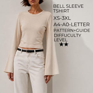 May include: A beige long-sleeve t-shirt with wide bell sleeves and a crew neckline. Text on the right reads: BELL SLEEVE TSHIRT, XS-3XL, A4-A0-LETTER, PATTERN+GUIDE, DIFFUCULTY LEVEL, and two star icons. The shirt is paired with white jeans and a black belt.