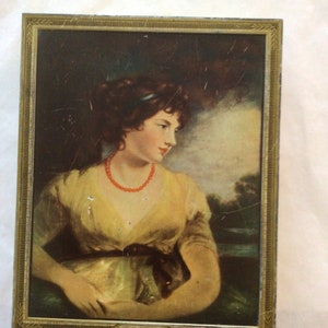 May include: A framed portrait of a woman with dark hair wearing a yellow dress and a red beaded necklace. The portrait is set against a background of a landscape with a river and trees.