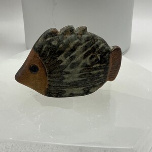 May include: A ceramic fish figurine with brown and gray glaze. The fish has a textured surface and a black eye.