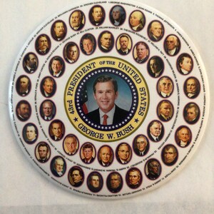 May include: A white circular button featuring a colourful image of the presidents of the United States. The button includes a seal with the words "President of the United States" and "George W. Bush".