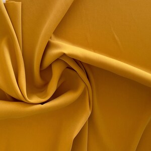 May include: A close-up of a smooth, mustard yellow fabric. The fabric is folded and draped, creating soft folds and curves.