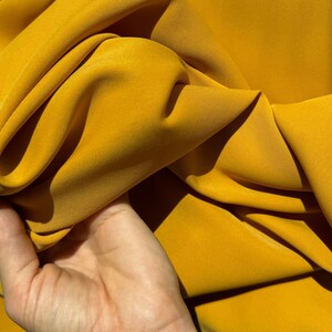May include: A close-up of a bright yellow fabric, showing its texture and drape. The fabric is smooth and silky, with a slight sheen.