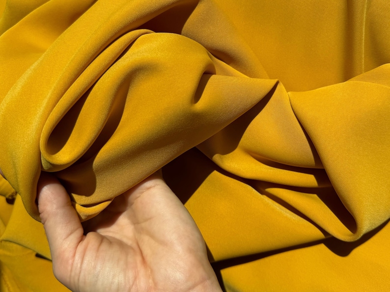 May include: A close-up of a bright yellow fabric, showing its texture and drape. The fabric is smooth and silky, with a slight sheen.