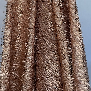 May include: Close-up of a rose gold fabric with a textured, sequined design. The fabric has a raised, spiky texture.
