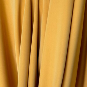 May include: Close-up of a smooth, yellow fabric with folds and creases. The fabric has a soft, luxurious feel.
