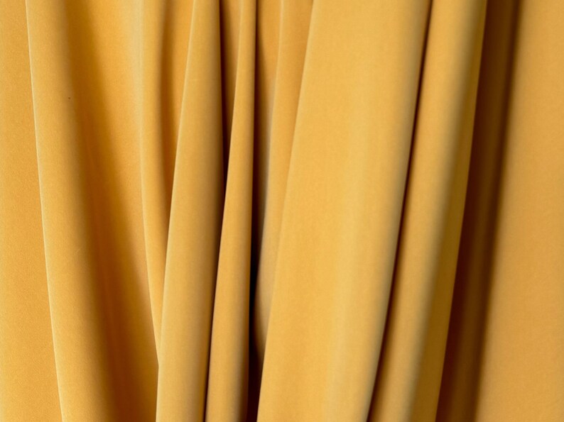May include: Close-up of a smooth, yellow fabric with folds and creases. The fabric has a soft, luxurious feel.