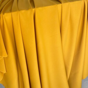 May include: A close-up of a yellow fabric, folded and draped over a surface. The fabric has a smooth, even texture and a rich, golden hue.