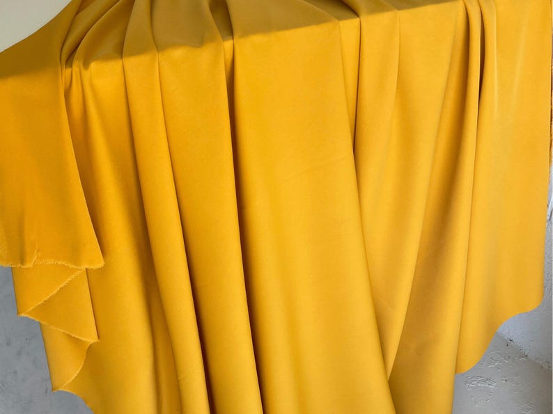 May include: A close-up of a yellow fabric, folded and draped over a surface. The fabric has a smooth, even texture and a rich, golden hue.
