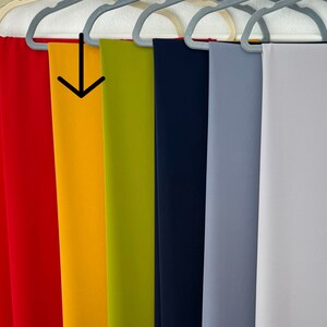 May include: A row of seven fabric swatches hanging on hangers. The swatches are in the following colors: red, yellow, green, navy blue, light blue, and white.