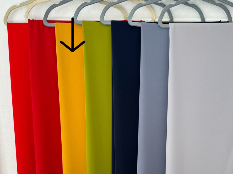 May include: A row of seven fabric swatches hanging on hangers. The swatches are in the following colors: red, yellow, green, navy blue, light blue, and white.