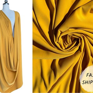 May include: A mustard yellow fabric draped over a mannequin. The fabric is soft and flowing, with a slight sheen. The fabric is shown in a close-up, with the folds and wrinkles visible. The text "FAST SHIPPING" is visible in the lower right corner of the image.
