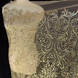 May include: Gold glitter fabric with a damask pattern. The fabric is sheer and has a delicate, intricate design.