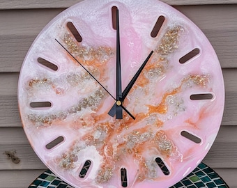 May include: Pink resin clock with gold and white glitter accents. The clock has a round face with black hands and Roman numeral markings.