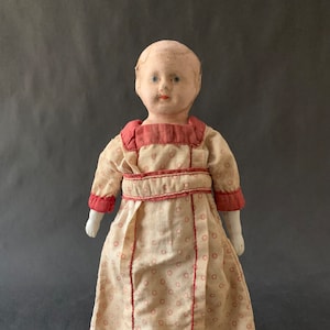 May include: Antique porcelain doll with painted blue eyes and a red and white polka dot dress.