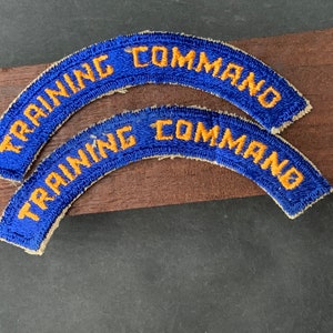 Puede incluir: Dos parches de tela azul y blanco con el texto "TRAINING COMMAND" en letras amarillas.