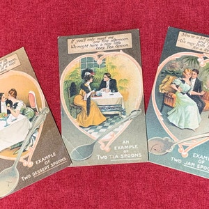 May include: Three vintage postcards with illustrations of couples enjoying a meal. Each postcard features a different type of spoon: dessert, tea, and jam. The text on the postcards reads: "True love in due course its desserts must get soon, Then let us take our time Dessert spoon", "If you'll only meet me one fine afternoon We might have a nice cosy Tea Spoon", and "You're a bit of Real Jam and I hope very soon, We may both have the chance for a Real Jam Spoon".