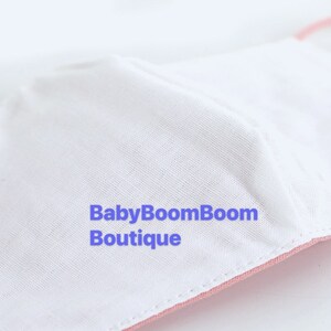 May include: Close-up of a pink and white fabric face mask with the text "BabyBoomBoom Boutique" printed on the white fabric.