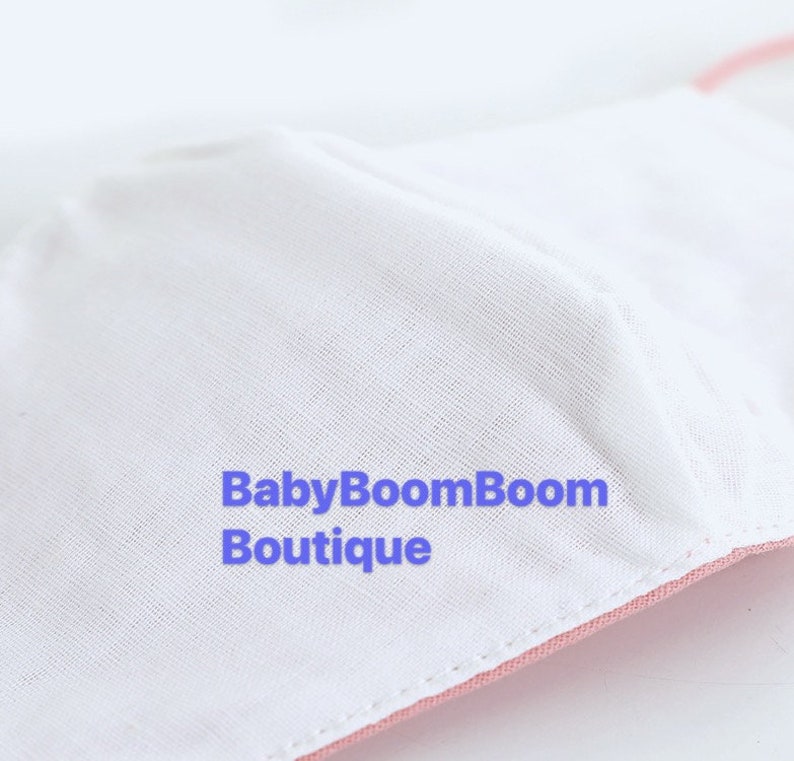 May include: Close-up of a pink and white fabric face mask with the text "BabyBoomBoom Boutique" printed on the white fabric.