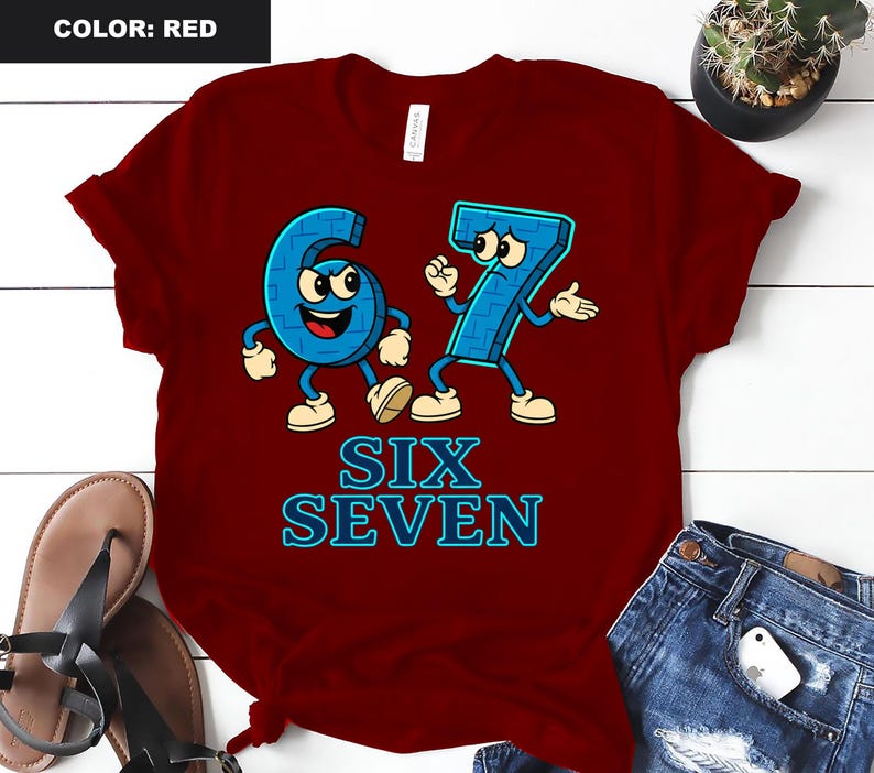 May include: A red t-shirt featuring the numbers six and seven as cartoon characters in blue with white accents. The text "SIX SEVEN" is displayed in blue below the characters. The shirt is a solid red color.