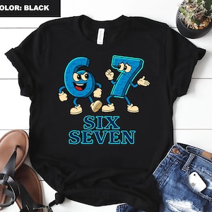 May include: Black t-shirt featuring the numbers six and seven as cartoon characters in blue with facial expressions and limbs. The words "SIX SEVEN" are printed in a blue, outlined font below the numbers. The shirt is displayed on a white wooden surface.