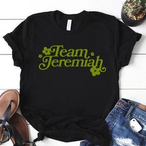 May include: Black t-shirt with the text "Team Jeremiah" in green with small flower graphics.
