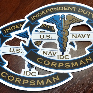 May include: Two white, blue, and gold stickers with the text "Independent Duty Corpsman U.S. Navy IDC" and a caduceus symbol.