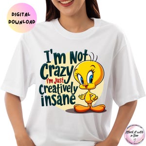 May include: White t-shirt featuring the cartoon character Tweety Bird with the text "I'm Not Crazy, I'm Just Creatively Insane." The design includes a yellow Tweety Bird on a yellow circle. The words are in dark green and blue.