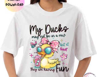 May include: White t-shirt featuring a cartoon duck wearing sunglasses and a pink bow, holding a pink drink. The text reads "My Ducks may not be in a row but at least they are having Fun." A digital download graphic.
